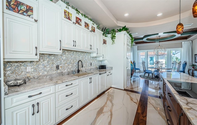 kitchen featuring pendant lighting, white cabinetry, sink, backsplash, and light stone counters