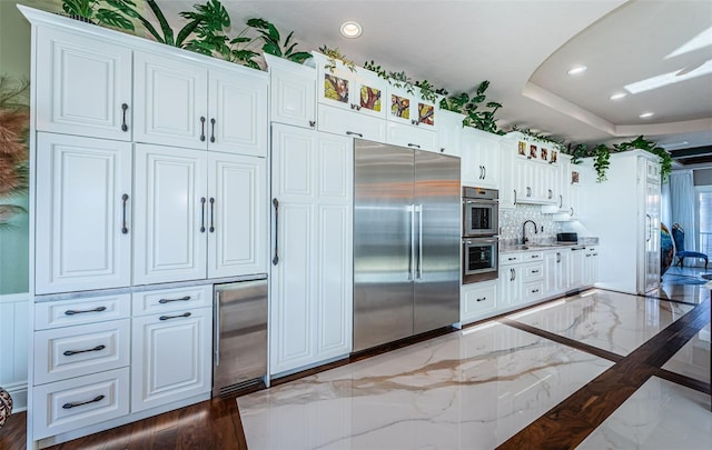 kitchen with sink, appliances with stainless steel finishes, wine cooler, a tray ceiling, and white cabinets