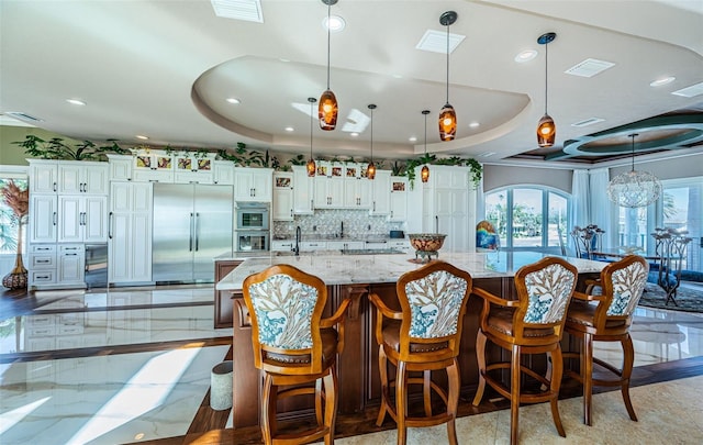 kitchen with a breakfast bar, decorative light fixtures, a large island with sink, a tray ceiling, and stainless steel appliances