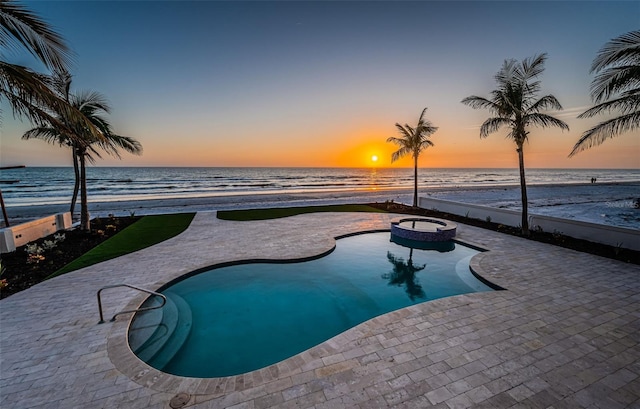 pool at dusk with a water view, a view of the beach, and a patio