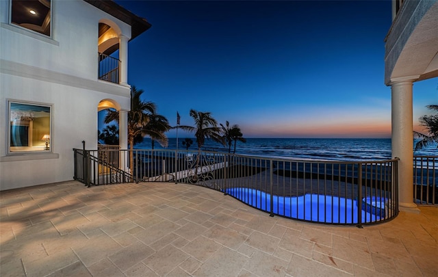 patio terrace at dusk with a balcony, a water view, and a view of the beach