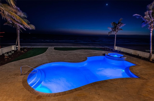 pool at dusk featuring an in ground hot tub, a patio, and a water view