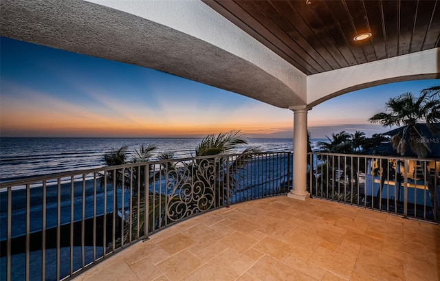 balcony at dusk featuring a view of the beach and a water view