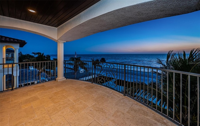 balcony at dusk featuring a water view and a view of the beach