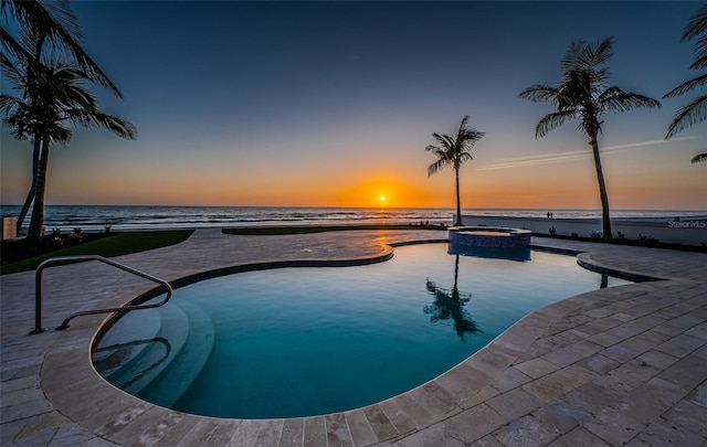 pool at dusk with an in ground hot tub, a water view, and a patio