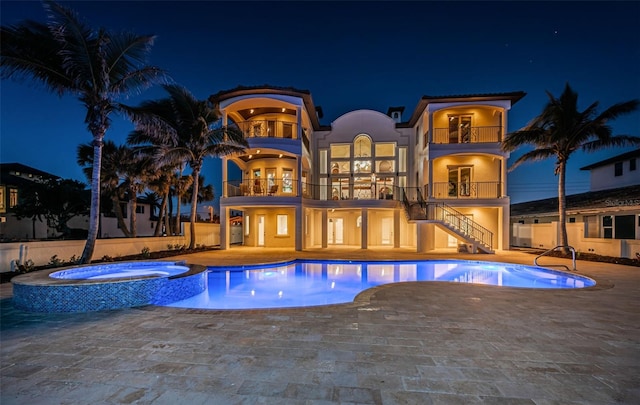 pool at night featuring an in ground hot tub and a patio area