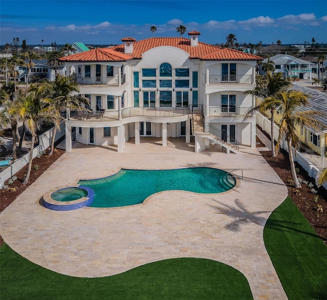 rear view of house with a patio, a balcony, and a pool with hot tub