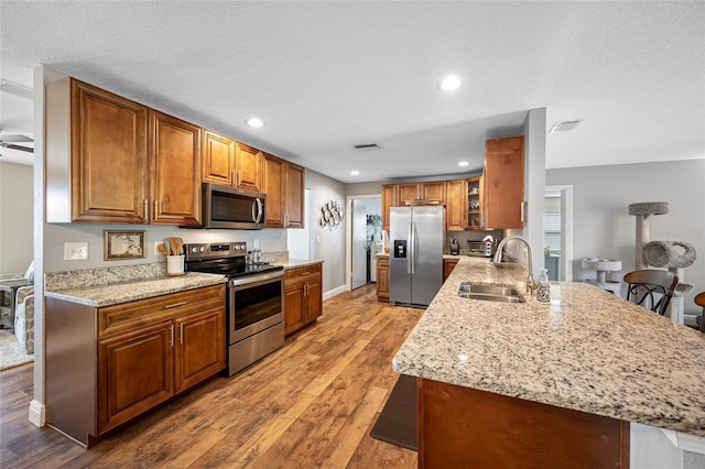 kitchen featuring a kitchen bar, sink, light stone counters, kitchen peninsula, and stainless steel appliances