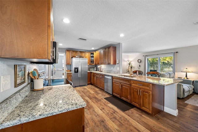 kitchen with stainless steel appliances, light stone countertops, dark wood-type flooring, and kitchen peninsula