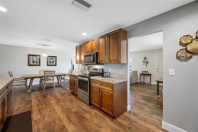 kitchen with dark hardwood / wood-style flooring, light stone countertops, stainless steel appliances, and a textured ceiling