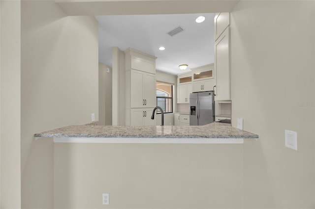 kitchen featuring light stone counters, white cabinetry, stainless steel fridge, and kitchen peninsula