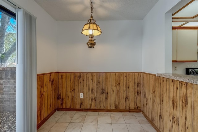 unfurnished dining area with a textured ceiling, wainscoting, and wooden walls