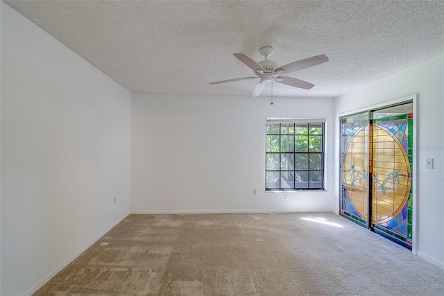 empty room with a textured ceiling, carpet floors, a ceiling fan, and baseboards