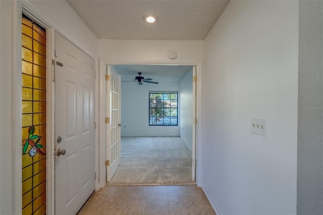 hallway with light colored carpet, a textured ceiling, baseboards, and light tile patterned floors