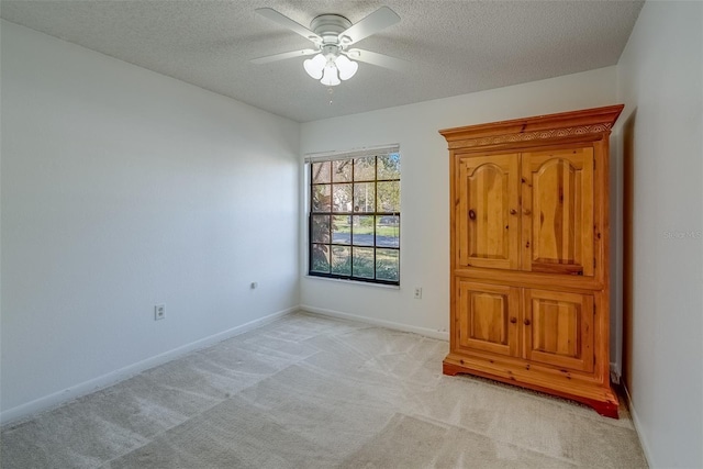 unfurnished room with a ceiling fan, light colored carpet, a textured ceiling, and baseboards