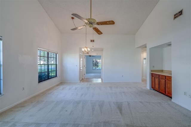 spare room featuring visible vents, a towering ceiling, light carpet, baseboards, and ceiling fan with notable chandelier