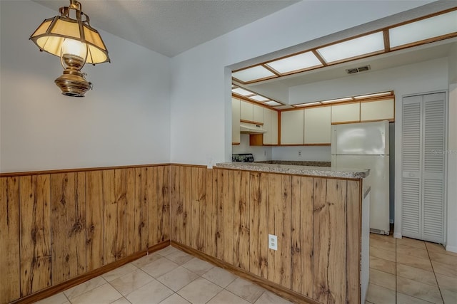 kitchen with light tile patterned flooring, a wainscoted wall, a peninsula, visible vents, and freestanding refrigerator