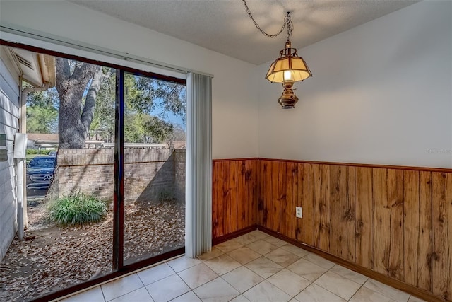 entryway with a wainscoted wall, light tile patterned floors, a textured ceiling, and wooden walls