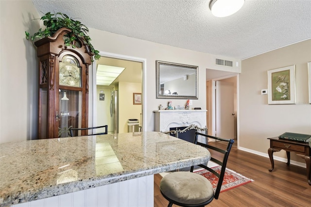 kitchen with a breakfast bar area, dark hardwood / wood-style floors, light stone countertops, and a textured ceiling