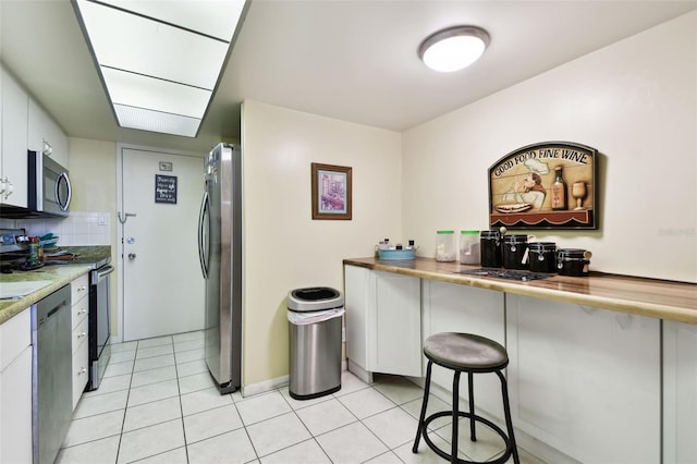 kitchen with stainless steel appliances, white cabinetry, tasteful backsplash, and light tile patterned flooring