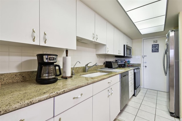 kitchen with light tile patterned floors, sink, white cabinetry, stainless steel appliances, and light stone counters