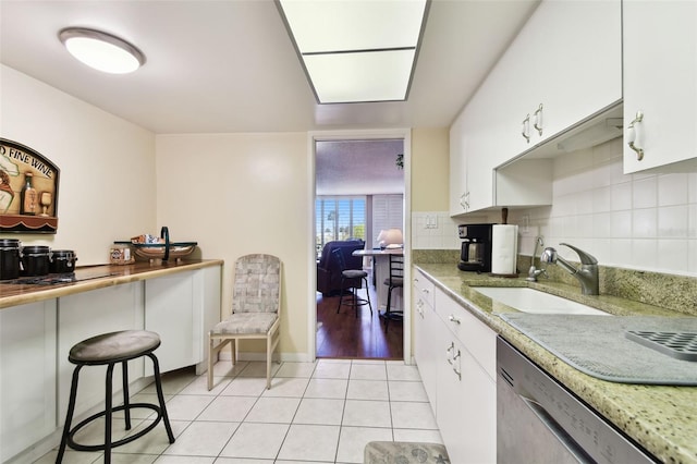 kitchen with sink, white cabinets, decorative backsplash, stainless steel dishwasher, and light tile patterned floors