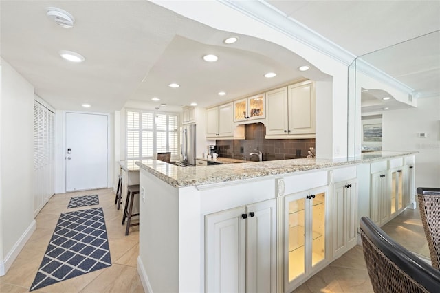 kitchen featuring light stone counters, stainless steel fridge, ornamental molding, and tasteful backsplash