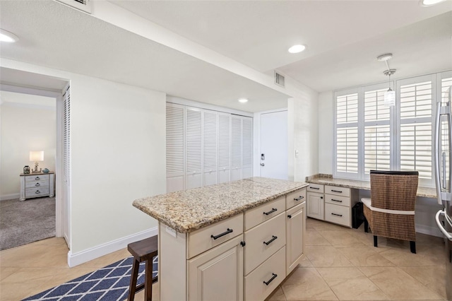 kitchen with built in desk, a breakfast bar area, a center island, light tile patterned floors, and light stone countertops