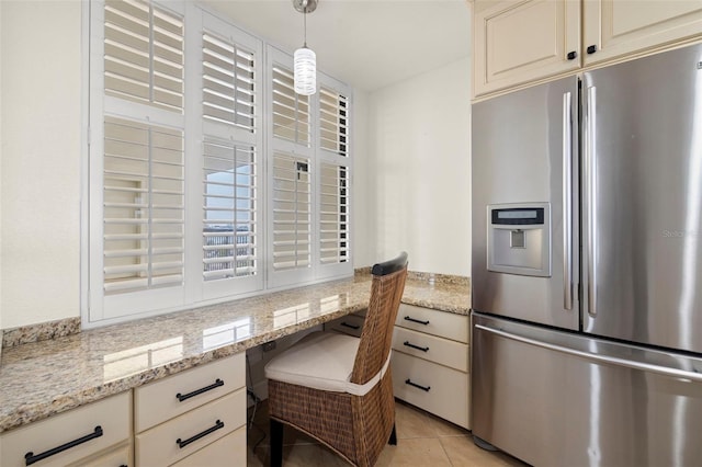 kitchen with pendant lighting, built in desk, light tile patterned floors, stainless steel refrigerator with ice dispenser, and light stone countertops