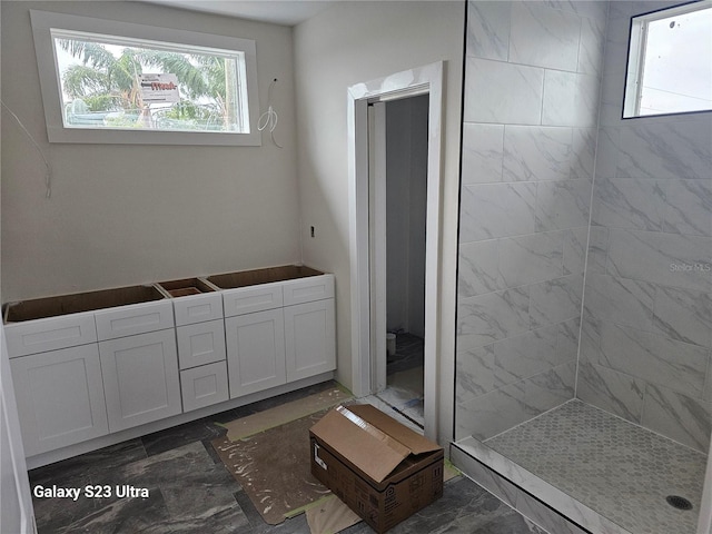 bathroom featuring a wealth of natural light, marble finish floor, and a tile shower