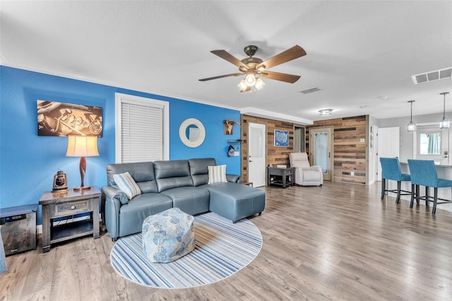 living room with wood-type flooring, wooden walls, ceiling fan, and a textured ceiling