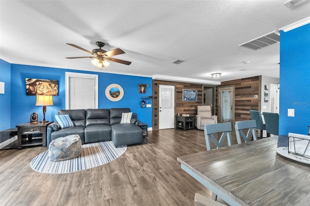 living room featuring crown molding, ceiling fan, hardwood / wood-style floors, wooden walls, and a textured ceiling