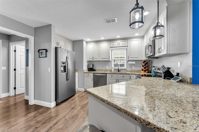 kitchen with appliances with stainless steel finishes, pendant lighting, sink, white cabinets, and light stone counters