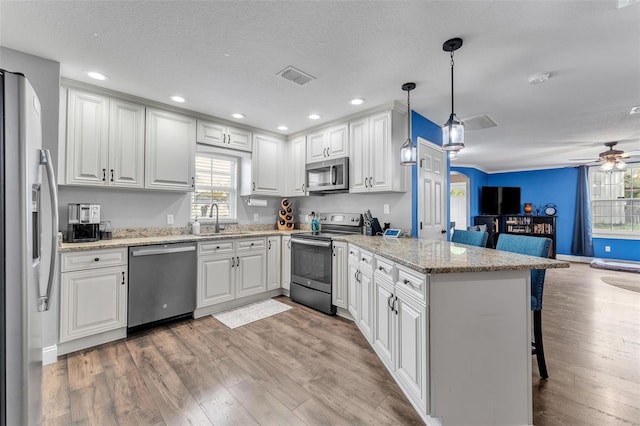 kitchen featuring a breakfast bar area, decorative light fixtures, appliances with stainless steel finishes, kitchen peninsula, and white cabinets