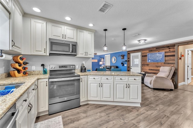 kitchen featuring light hardwood / wood-style flooring, wooden walls, stainless steel appliances, decorative light fixtures, and kitchen peninsula