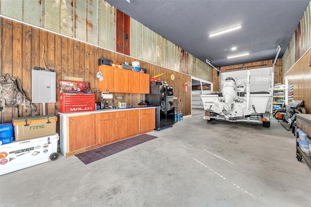 garage featuring black fridge with ice dispenser, a workshop area, electric panel, and wood walls