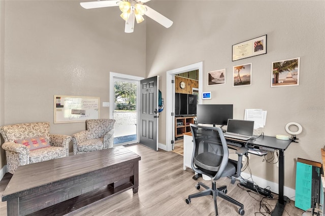 office area featuring a towering ceiling, ceiling fan, and light wood-type flooring