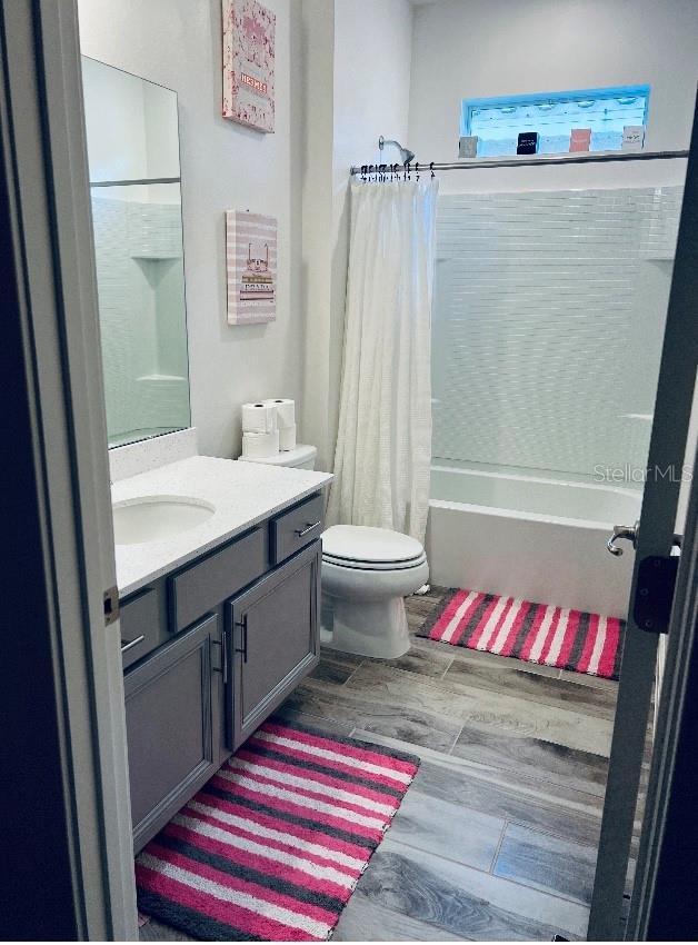 full bathroom featuring wood-type flooring, toilet, shower / tub combo with curtain, and vanity