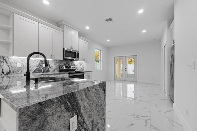 kitchen with appliances with stainless steel finishes, stone countertops, white cabinetry, sink, and french doors