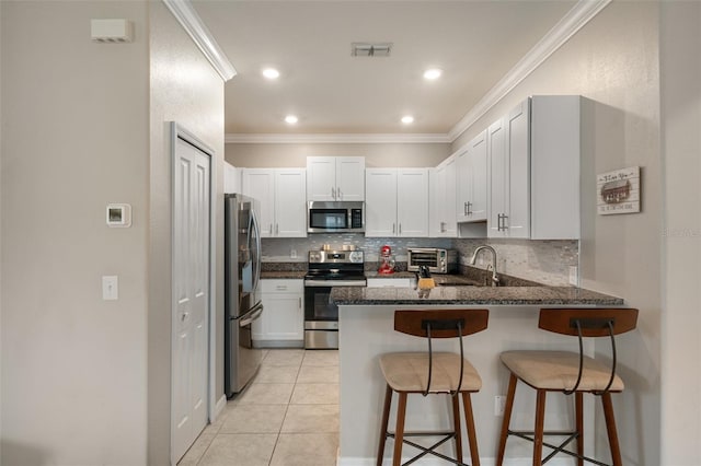 kitchen with appliances with stainless steel finishes, a kitchen bar, kitchen peninsula, and white cabinets