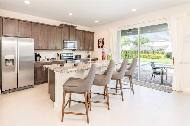 kitchen featuring appliances with stainless steel finishes, an island with sink, sink, a breakfast bar area, and light stone countertops