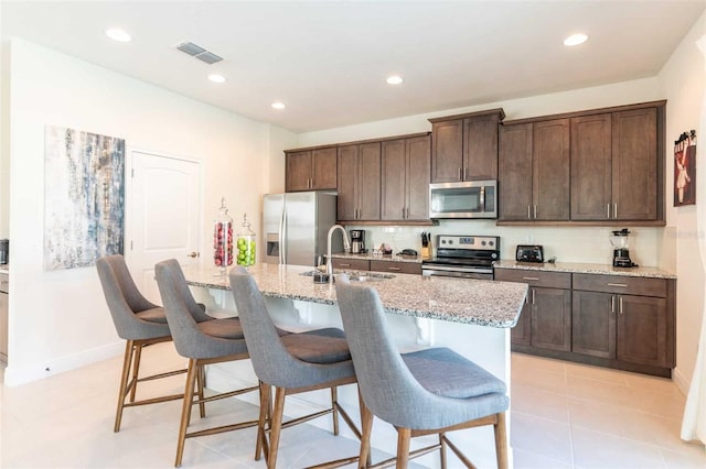 kitchen featuring sink, a breakfast bar area, light stone counters, stainless steel appliances, and a kitchen island with sink