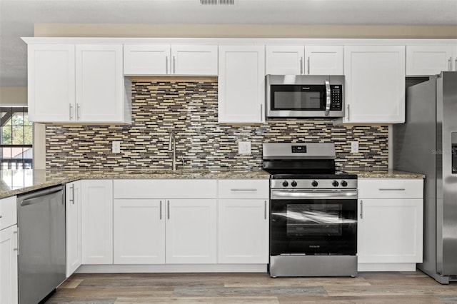 kitchen featuring sink, light stone counters, appliances with stainless steel finishes, decorative backsplash, and white cabinets