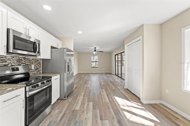 kitchen with appliances with stainless steel finishes, white cabinetry, backsplash, light stone countertops, and light hardwood / wood-style floors