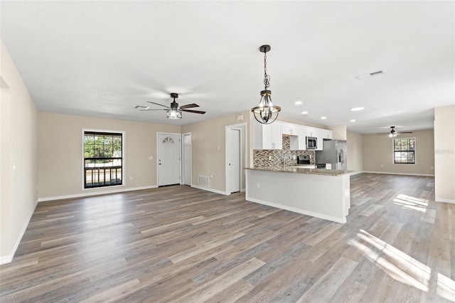 kitchen featuring pendant lighting, appliances with stainless steel finishes, white cabinetry, decorative backsplash, and kitchen peninsula