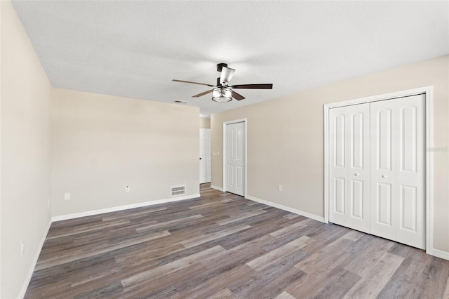 unfurnished bedroom with multiple closets, ceiling fan, wood-type flooring, and a textured ceiling