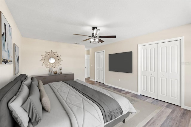 bedroom with two closets, a textured ceiling, ceiling fan, and light wood-type flooring