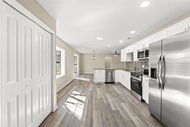 kitchen featuring white cabinetry, decorative light fixtures, kitchen peninsula, stainless steel appliances, and decorative backsplash