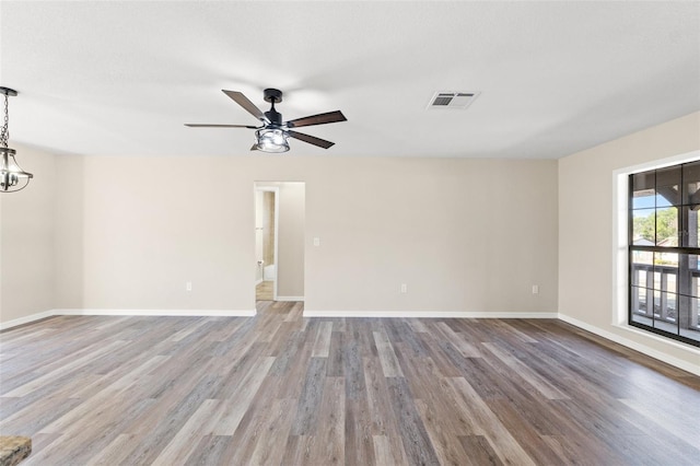 empty room with ceiling fan with notable chandelier and wood-type flooring