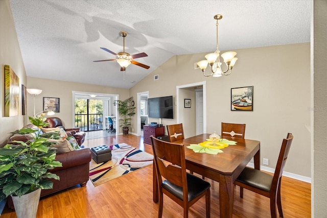 dining space with ceiling fan with notable chandelier, wood-type flooring, a textured ceiling, and vaulted ceiling